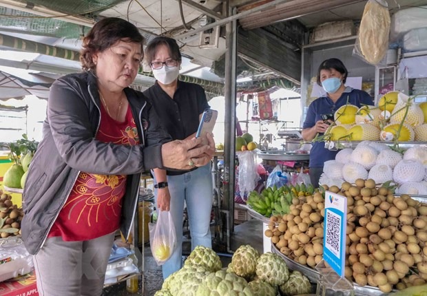 Người d&amp;acirc;n sử dụng điện thoại th&amp;ocirc;ng minh để thanh to&amp;aacute;n tiền mua b&amp;aacute;n h&amp;agrave;ng h&amp;oacute;a ở chợ
